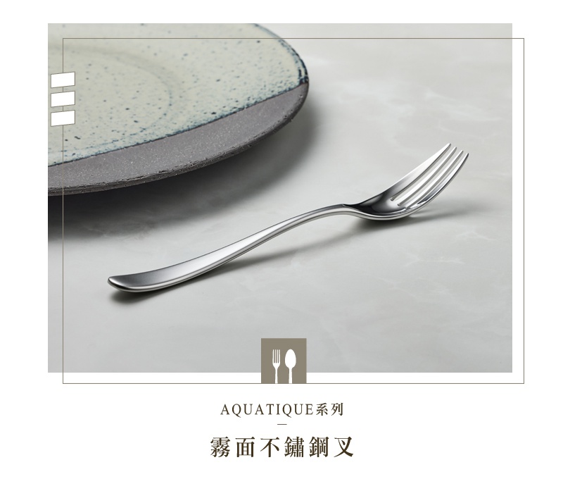 一支霧面不鏽鋼叉，置於淺色桌面，背景為部分盤子
