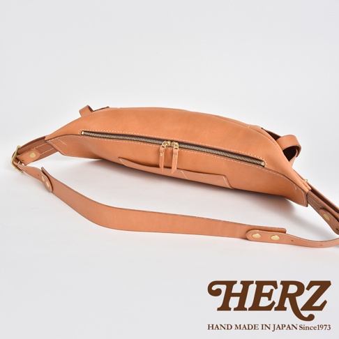 HERZ 職人手作皮革大容量斜背包，淺棕色皮革材質，側邊視角，展示雙拉鍊主袋和可調節肩背帶。