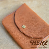 職人手作皮革小物收納袋，採用天然皮革製成，呈現溫潤的棕色調，表面有細緻紋理。鈕扣式設計，方便開合。