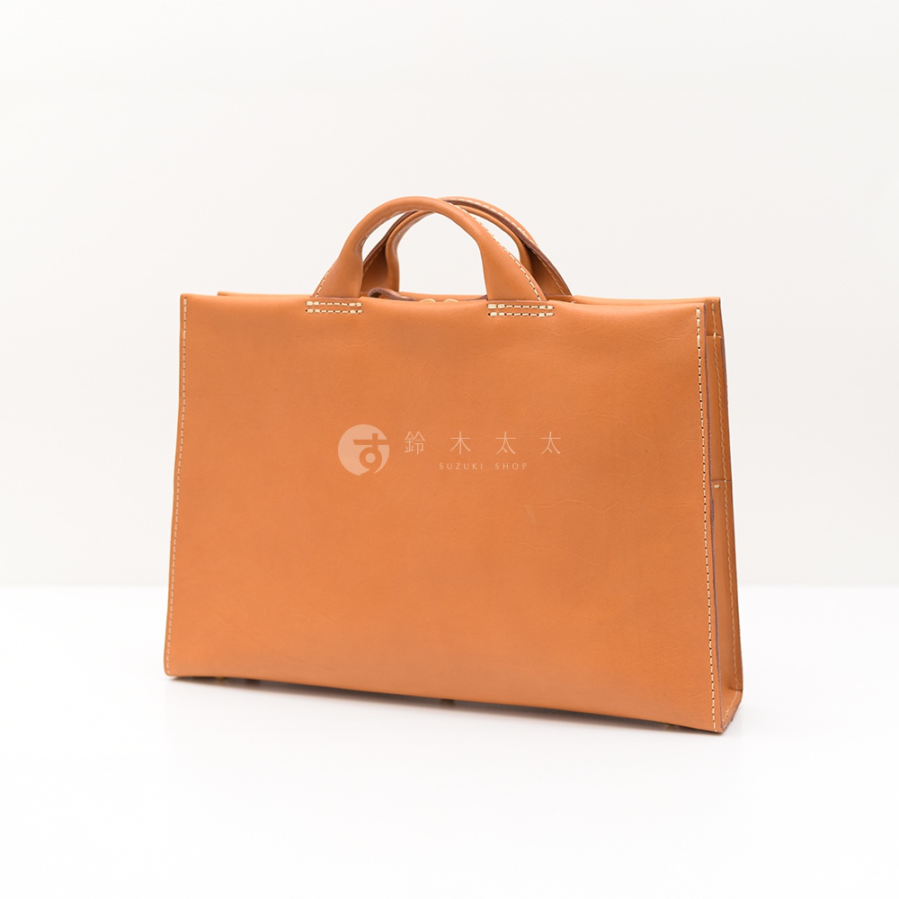 日本HERZ 職人手作皮革簡約商務公事包 BW-104，使用駱駝色皮革製作，包款正面印有 SUZUKI SHOP 標誌，採用簡約設計搭配提把，整體風格商務且質感良好。