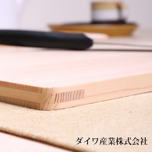 日本製超薄檜木砧板，淺木色，表面紋理清晰，邊緣處可見榫接結構。背景模糊，有黑色刀柄和白色、黃色器皿。