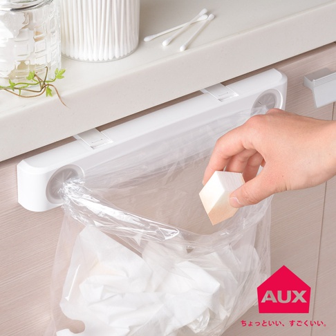 白色塑膠掛架，下方懸掛著一個透明塑膠袋，袋內裝有白色紙巾。一隻手正將方形的粉撲放入塑膠袋中。