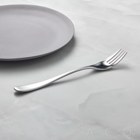 霧面不鏽鋼晚餐叉，靠近灰色霧面盤子，放在大理石紋桌面上，叉子呈現流線型設計，叉頭有三根叉齒。