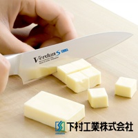 VERDUN S 不鏽鋼水果刀，刀身有「Verdun S」和「MoV STAINLESS STEEL MADE IN JAPAN / SHIMOMURA」字樣，正在切分塊狀的黃油，刀刃鋒利，背景為木質砧板，右下角有「下村工業株式會社」的標誌。