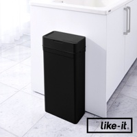 一個黑色、長方形的按壓式垃圾桶，帶有密封蓋，放置在白色櫥櫃旁的地板上。