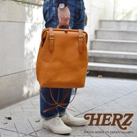 職人手作皮革後背包 R-143，採用天然皮革製作，呈現溫潤的焦糖棕色。包款設計簡約，配有雙扣環開合，適合日常攜帶。