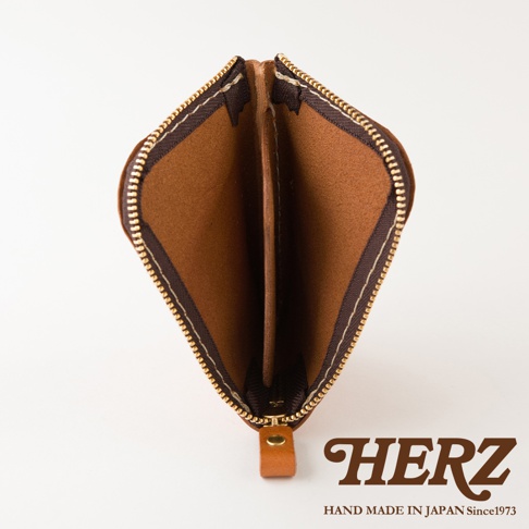這是一款日本HERZ手工製作的棕色皮革迷你零錢包，從上方視角拍攝，展現出錢包內部設有分隔層的結構。錢包邊緣飾有金色金屬拉鍊，底部連接著一個皮革製成的拉鍊頭，整體呈現出簡約而精緻的職人手作風格。
