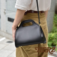 黑色皮革製作的職人手作單肩兩用拱型手袋，配有手提握把和可調節的長肩帶。包身線條流暢，頂部有縫線細節，底部設有金屬腳釘。