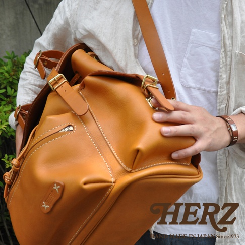 職人手作皮革復古風旅行後背包，採用光滑的天然棕色皮革，配有黃銅色金屬扣環和拉鍊。包身線條簡潔，縫線細緻，展現高品質的工藝。