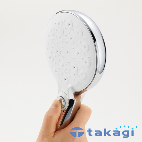 一隻手持著Takagi KIREIST真淨水水霧蓮蓬頭，特寫展示圓形噴頭上的細緻出水孔排列與握把上的銀色開關按鈕，整體呈現白色與金屬質感相間的設計。