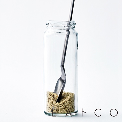 日製不鏽鋼小長勺，勺頭呈扁平狀，置於透明玻璃瓶中，瓶內裝有淺黃色顆粒狀物質。