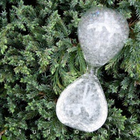 透明玻璃製成的泡泡沙漏，沙漏內充滿細小的白色氣泡。沙漏置於綠色針葉植物背景上。