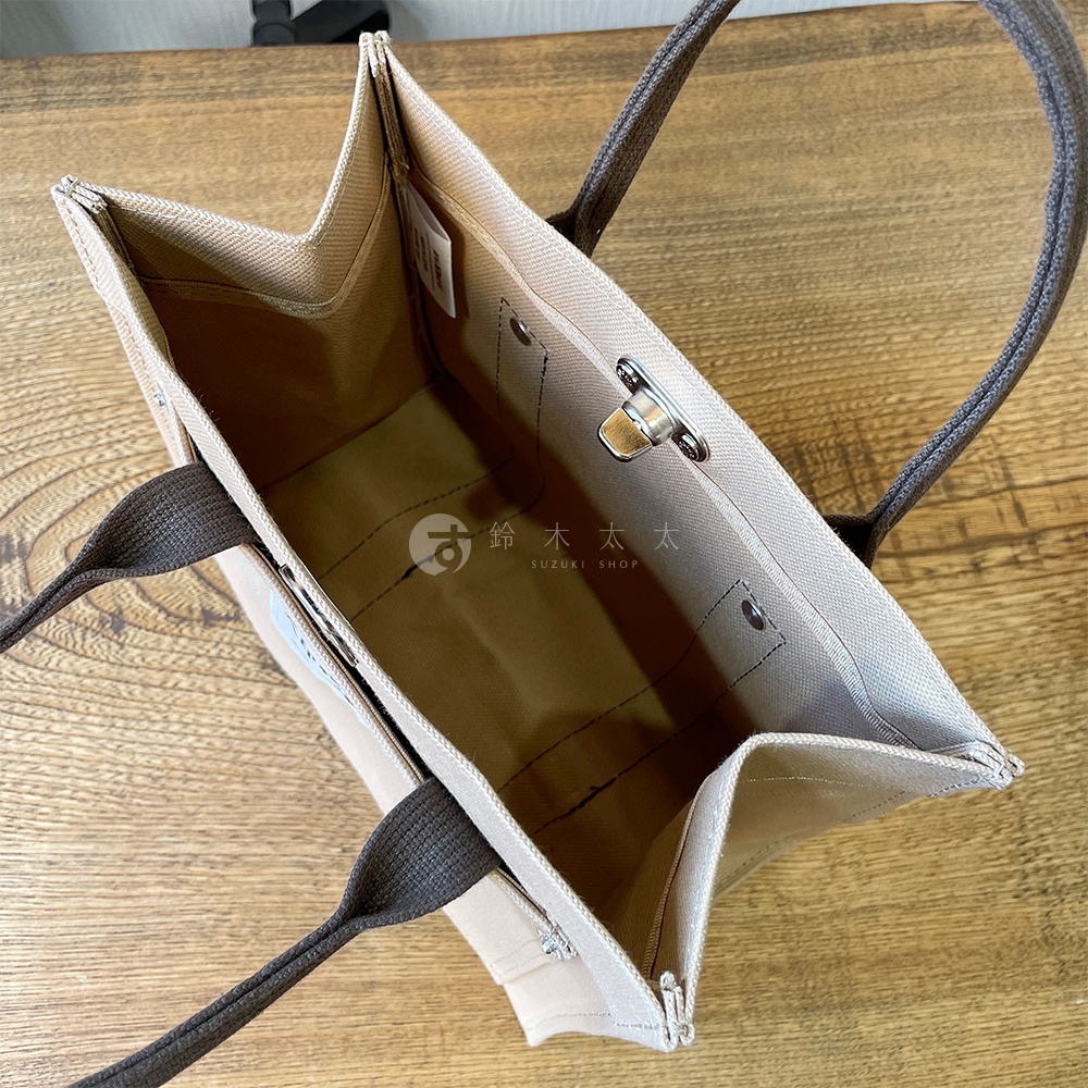 開啟的米白色純棉帆布迷你托特包，內裡為卡其色，配有深棕色提把，包包側面有鈕扣及金屬鎖扣。