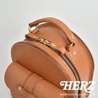 職人手作皮革迷你後背包，採用天然皮革材質，呈現焦糖棕色調。包款圓潤，配有金色拉鍊、黃銅色五金配件及一體式提把，側邊設計有外置收納袋。