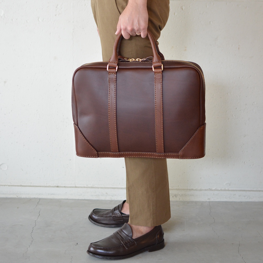 職人手作深棕色皮革Organ商務公事包，配有金色拉鍊和同色系縫線，包身兩側有皮革加固設計，手柄為雙提把。