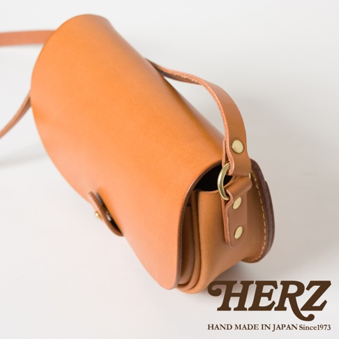 職人手作皮革迷你馬鞍包，淺棕色，圓潤弧形包身，附有短提把及可調節長度的斜背帶，黃銅金屬扣件，簡約設計。