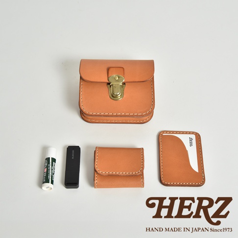 皮革經典腰包，以天然鞣製皮革製成，帶有黃銅釦環。旁邊展示一個小型皮革零錢包、一個USB隨身碟、一支護唇膏和一個卡夾。