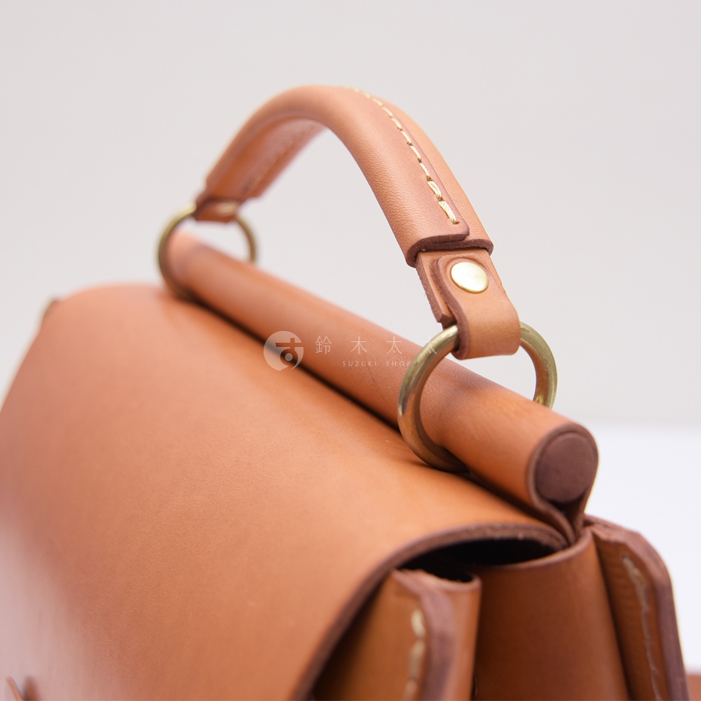 精緻皮革包的提把與金屬配件特寫，上方有品牌日文與英文Logo。