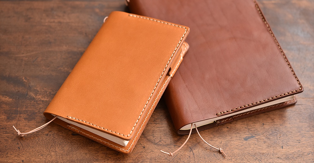 兩個皮革手帳書套，一個淺棕色，一個深棕色，放在木桌上。