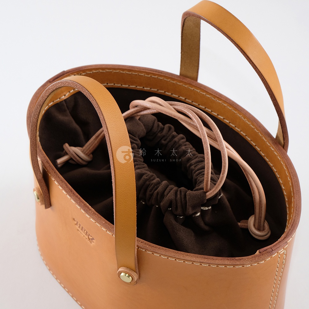 職人手作皮革束口手提包，淺棕色皮革材質，內部為深棕色束口袋，兩側有提把，包身有縫線細節。