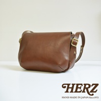 職人手作復古翻蓋郵差包，採用棕色皮革製成，配有金色金屬扣環和可調節肩帶。