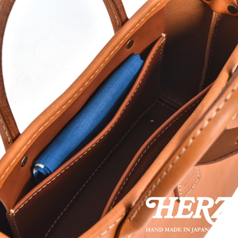 職人手作皮革迷你托特包 T-11，展示包包內部結構，一個藍色布料置於前側內袋中，包身為棕色牛皮材質，車縫線清晰，整體呈現簡約質感。