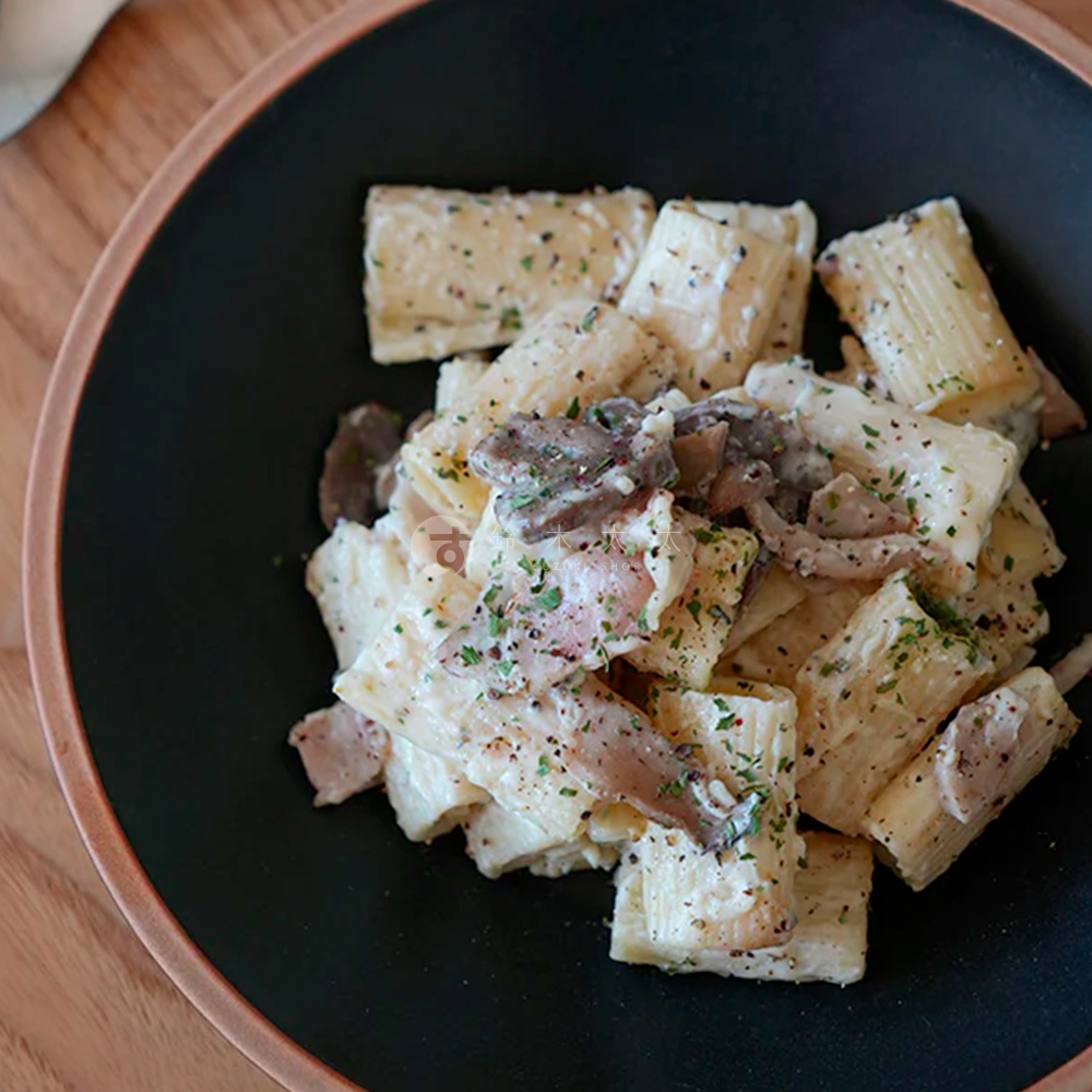 黑色陶瓷義大利麵盤盛著筆管麵，搭配濃郁奶油醬、香菇片及香草碎，呈現樸實的餐點畫面。