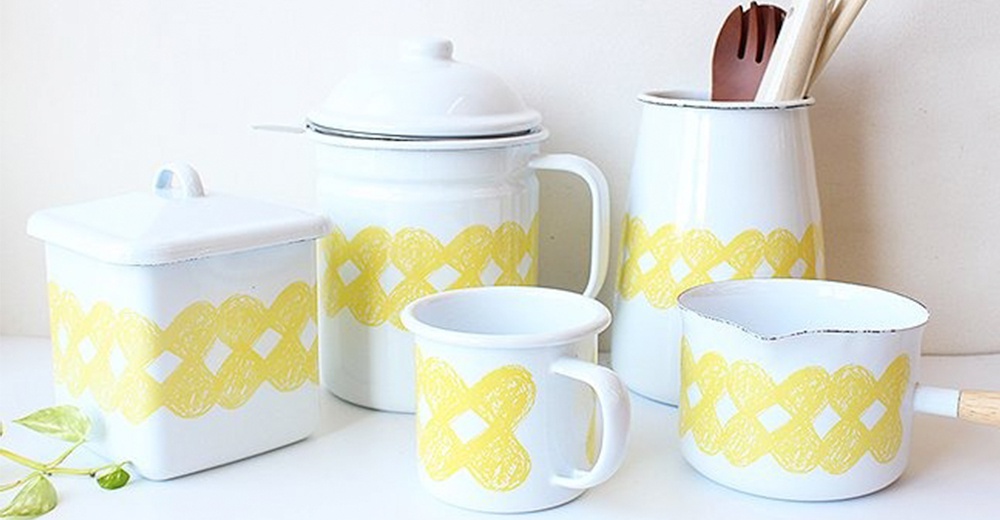 一套白色琺瑯廚具，包含方形儲物罐、附蓋水壺、馬克杯、湯鍋和廚具收納筒，皆飾有黃色編織紋路，部分帶有木質手柄。