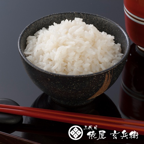 一碗盛滿的白色米飯，裝在一個黑色、帶有金色紋理的陶瓷碗中，旁邊放著一雙紅色的筷子。