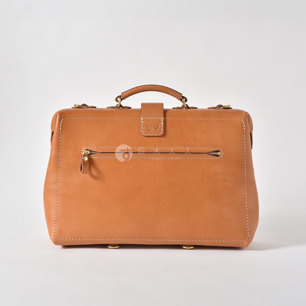 職人手作皮革軟式杜勒斯三用背包，採用天然棕褐色皮革製成，正面有一個拉鍊口袋，頂部有提把和金屬扣環，整體設計簡潔大方。