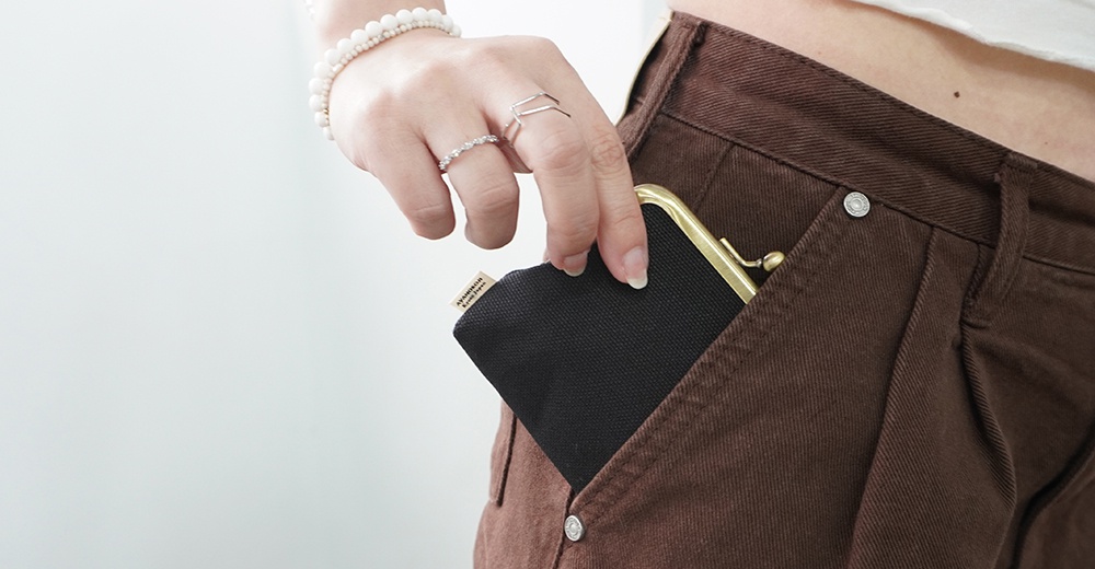 一名女性將一個帶有金色夾子的黑色帆布小錢包塞進棕色褲子的口袋裡。