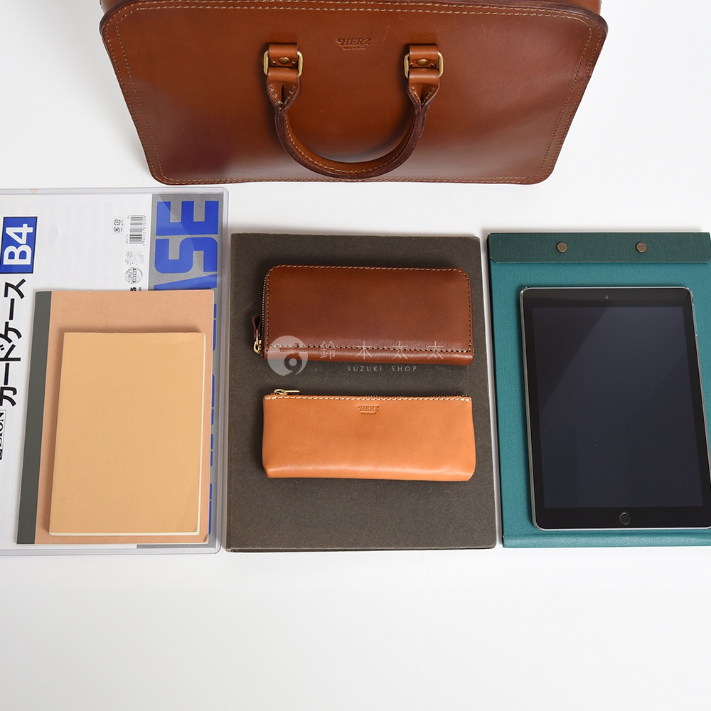 棕色皮革手提公事包，搭配同色系皮夾和筆袋，旁放有筆記本和平板電腦。
