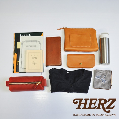 皮革製品組合：紅色皮革筆袋、棕色皮革長夾、淺棕色皮革手拿包、淺棕色皮革化妝包、黑色毛衣、金屬保溫杯、筆記本、雜誌。