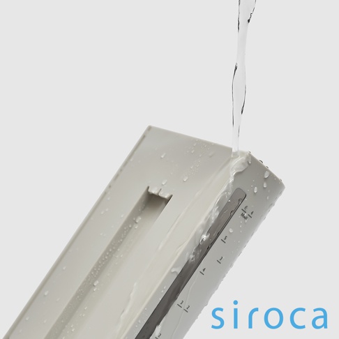 淺灰色 siroca SC-C2510 石臼式全自動研磨咖啡機的淺灰色水箱，有刻度標示，水正從上方注入，水滴濺落在機身上。