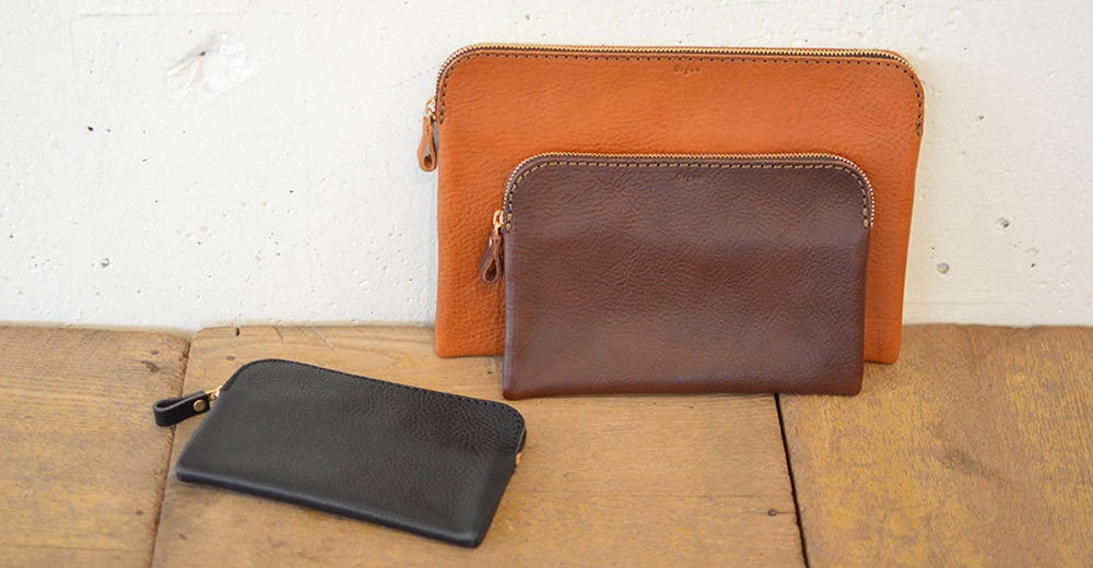 三個職人手作皮革Organ雙拉鍊收納袋，分別為黑色、棕色和橘色。材質為皮革，有明顯的紋理。拉鍊為金色，袋口有簡潔的縫線。