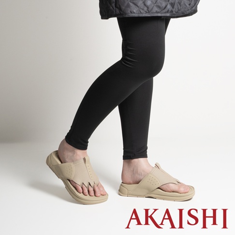 模特兒穿著AKAISHI品牌米色五指放鬆伸展拖鞋的側面視角，展示出特殊的五指分離設計與厚實鞋底，搭配黑色緊身褲，呈現舒適的休閒穿搭風格。