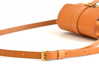 職人手作皮革皮扣單肩包，採用棕色皮革材質，設有可調節的皮革背帶和金屬皮扣，展現簡約時尚的風格。