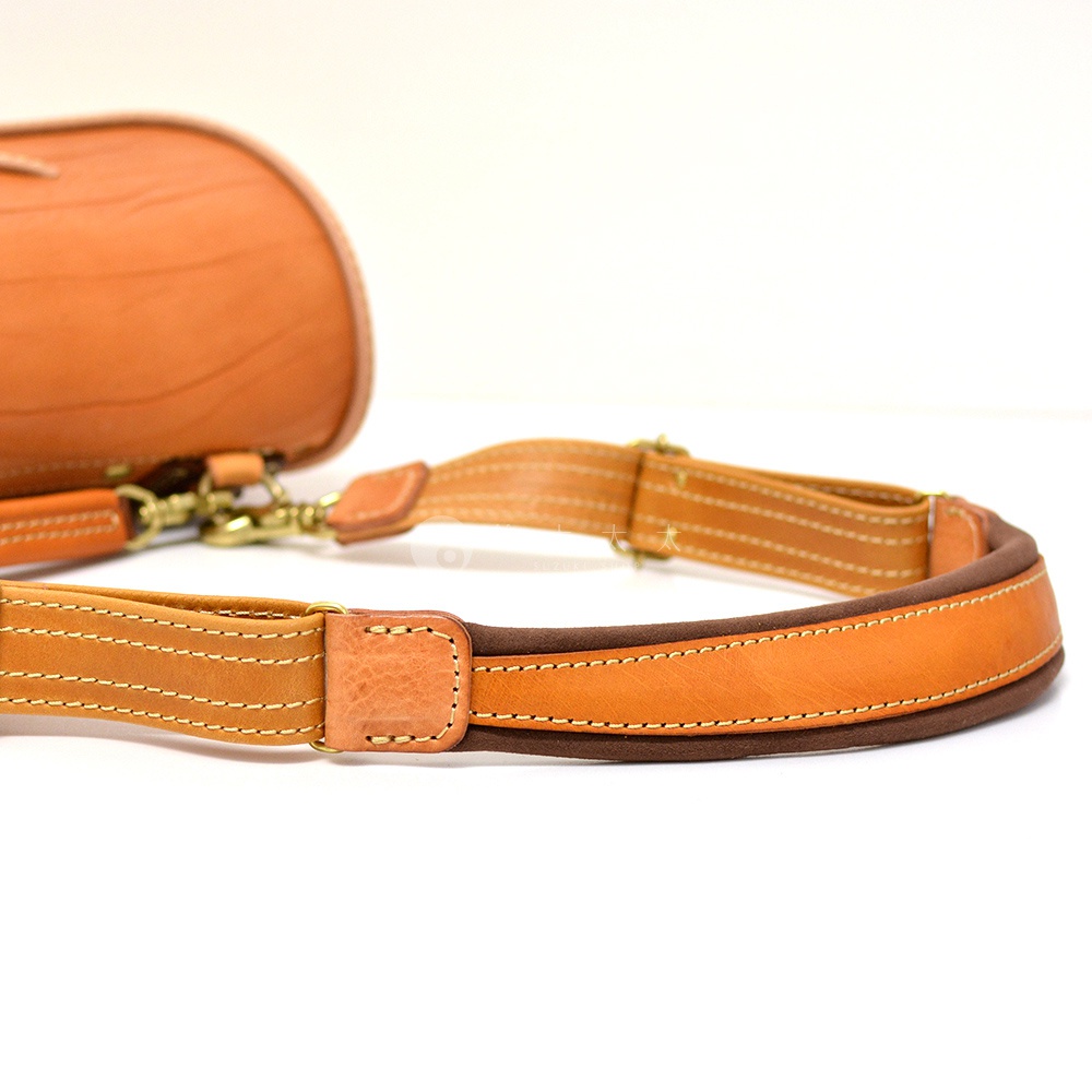 棕色皮革郵差包的肩帶特寫，展示了多層皮革拼接、縫線細節和金色金屬扣環。