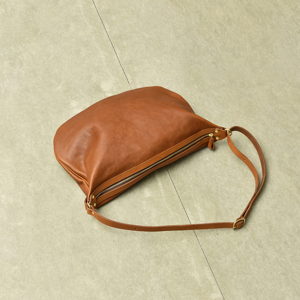 棕色皮革製成的職人手作Organ單肩半月包，包身柔軟，配有金色拉鍊和可調節式皮革背帶，整體呈自然的彎月形狀。