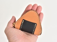 職人手作皮革零錢包，呈現三角飯糰造型，由淺棕色皮革與黑色皮革拼接而成，縫線清晰，搭配金色拉鍊。