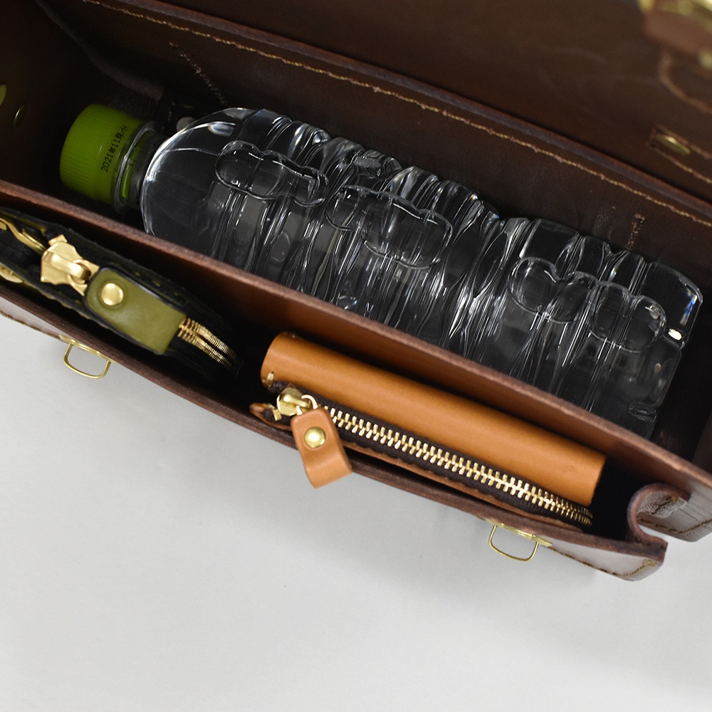 職人手作皮革雙扣兩用迷你肩背包 CW-67，展示內部收納，包含一個水瓶、一個綠色拉鍊零錢包及一個棕色長夾。