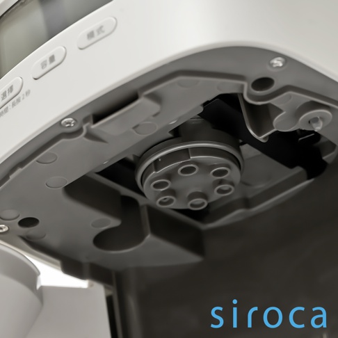 SC-C2510 石臼式全自動研磨咖啡機（淺灰色）的特寫，展示了機器底部淺灰色的塑膠外殼，以及露出部分黑色的研磨組件，其上有六個圓形孔槽。