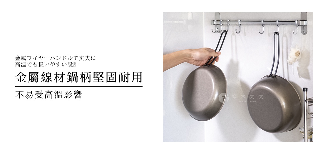 這張圖片展示了兩款掛在廚房牆上掛勾的深色鐵製平底鍋，平底鍋配有金屬線材把手，設計堅固且耐高溫，左側有一隻手正輕握住其中一個鍋具的把手。