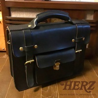 黑色皮革學院風兩用公事包，配有頂部提把、可調節側邊皮帶、前袋翻蓋及金色金屬鎖扣。