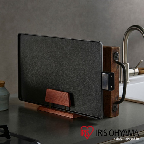 黑色輕薄方形電烤盤，帶有木質支架和金屬把手，放置於廚房檯面上，背景為水槽和灰色牆壁。