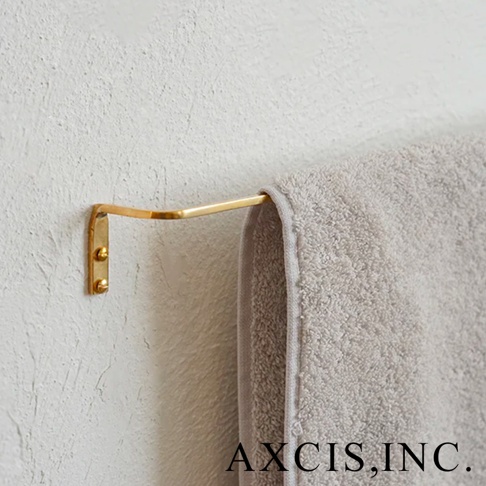 黃銅單桿毛巾架，L型設計，固定於白色紋理牆面，毛巾架呈現金色光澤，末端掛著一條淺灰色毛巾。