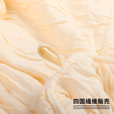 淺黃色舒芙蕾四季被，材質輕薄，表面呈現細膩的皺褶紋理，一條綁帶穿過布料邊緣的織帶。