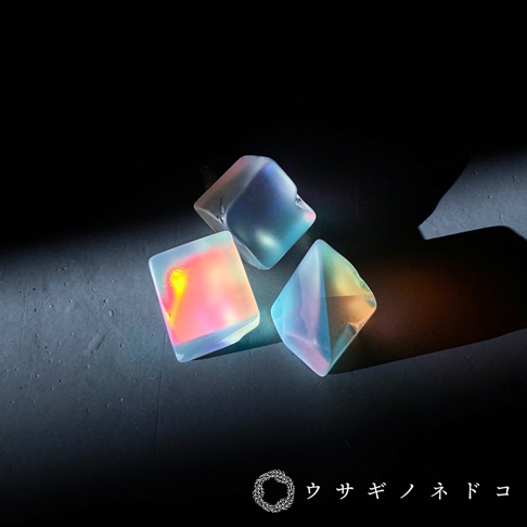 三顆合光稜鏡石，呈現立方體與多面體造型，表面光滑，散發著彩虹般的七彩光澤，從粉紅、黃色、藍色到綠色，在黑色背景下顯得格外耀眼。