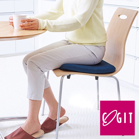 深藍色雙層蜂巢式凝膠坐墊，附有網狀布套，置於木質椅面上，一位女士坐著，手持白色馬克杯。