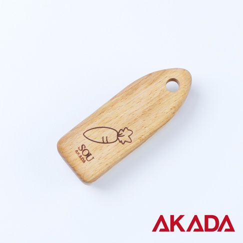 淺色木製蔬果刷，一端有孔，另一端刻有紅蘿蔔圖案及「SOU AKADA」標誌。